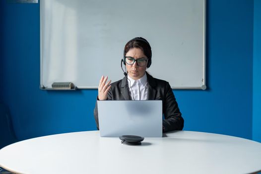 An angry woman in a headset is having an online conversation on a laptop in a conference room. Female boss scolding subordinates for a video call. Unsuccessful remote business negotiations