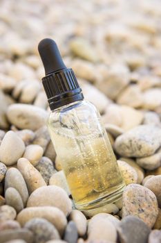 Cosmetic serum for the skin in a glass bottle. A bottle with an eyedropper on a pebble beach by the sea. Essences for skin care on the background of stones. The concept of natural cosmetics and SPA products.