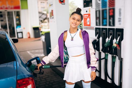 Cheerful young woman brunette filling her car with fuel at a gas station