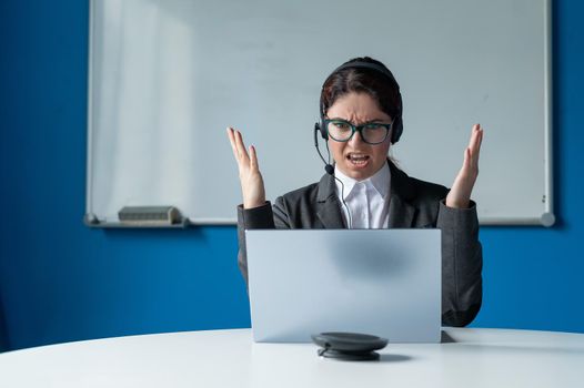 An angry woman in a headset is having an online conversation on a laptop in a conference room. Female boss scolding subordinates for a video call. Unsuccessful remote business negotiations