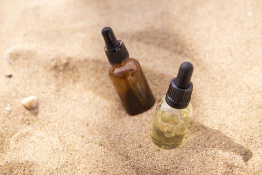 Cosmetic serum for the skin in a glass bottle. A bottle with a pipette on a sandy beach by the sea. Essences for skin care on a sandy background. The concept of natural cosmetics and SPA products.