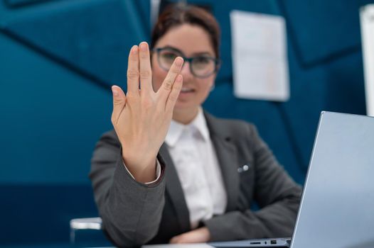 Business woman saying hello in Vulcan style while sitting at her desk in the office