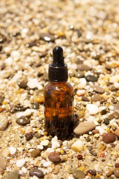 Cosmetic serum for the skin in a glass bottle. A bottle with an eyedropper on a pebble beach by the sea. Essences for skin care on the background of stones. The concept of natural cosmetics and SPA products.