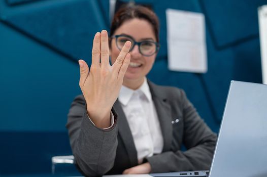 Business woman saying hello in Vulcan style while sitting at her desk in the office