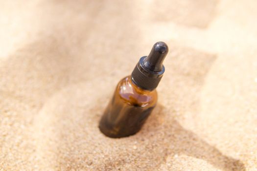 Cosmetic serum for the skin in a glass bottle. A bottle with a pipette on a sandy beach by the sea. Essences for skin care on a sandy background. The concept of natural cosmetics and SPA products.