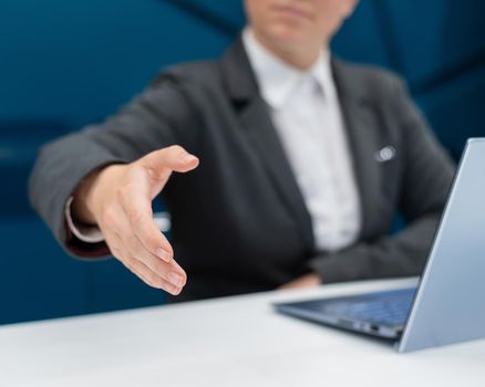 Faceless woman in a business suit holds out her hand for a handshake while sitting at a desk. Female boss makes a successful deal