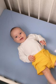 The baby is lying in his crib and looking at the camera . A happy child. Children's article. Copy Space