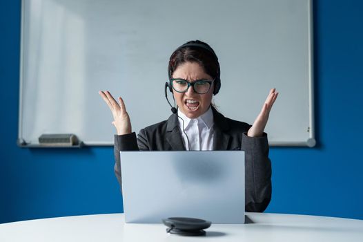 An angry woman in a headset is having an online conversation on a laptop in a conference room. Female boss scolding subordinates for a video call. Unsuccessful remote business negotiations