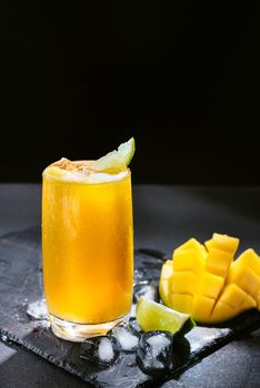 Mango juice on a dark background. Summer drink with ice and slices of mango and lime