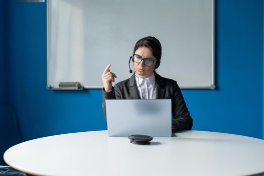 An angry woman in a headset is having an online conversation on a laptop in a conference room. Female boss scolding subordinates for a video call. Unsuccessful remote business negotiations