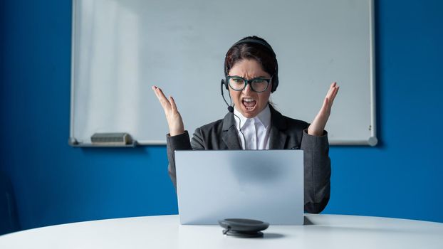 An angry woman in a headset is having an online conversation on a laptop in a conference room. Female boss scolding subordinates for a video call. Unsuccessful remote business negotiations