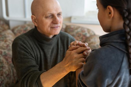 A hand of a granddaughter is holding a wrinkled hand of an old man symbolizing care, attention and unconditional love