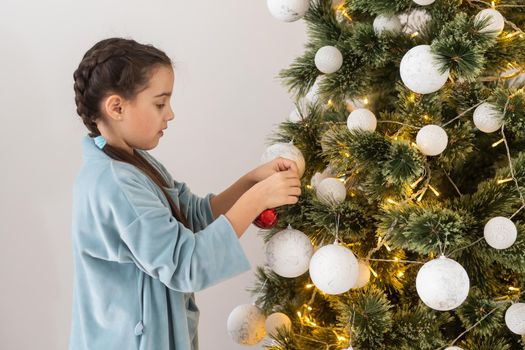 Little girl decorating christmas tree with toys and baubles. Cute kid preparing home for xmas celebration.