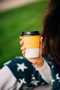 portrait of a young attractive woman in the park with a paper glass of coffee. Rest in the park