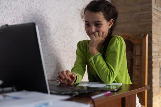 Child online. A little girl uses a laptop video chat to communicate learning while sitting at a table at home