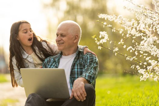 grandfather and granddaughter with laptop in the garden.