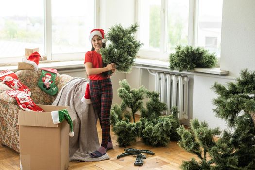 Photo of cute cheerful little girl makes an artificial Christmas tree wear santa hat indoors.