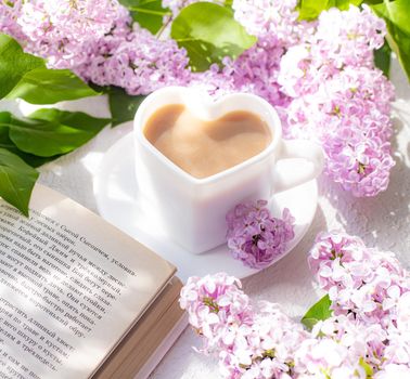 Cappuccino coffee in a cup and a branch of lilac on a white background with shadows . A hot drink. relax. The concept of cafeteria advertising. Article about cappuccino. Making cappuccino. Lilac branches. Spring. Copy space