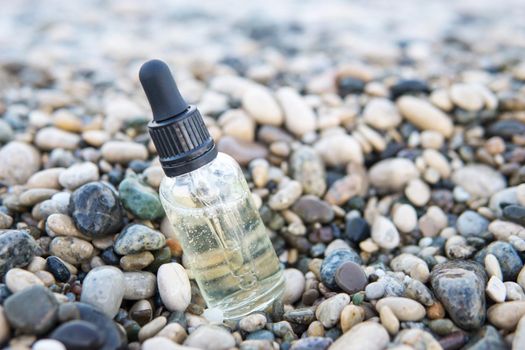 Cosmetic serum for the skin in a glass bottle. A bottle with an eyedropper on a pebble beach by the sea. Essences for skin care on the background of stones. The concept of natural cosmetics and SPA products.