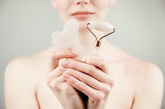 Caucasian woman holding pink roller massager and gouache scraper on white background