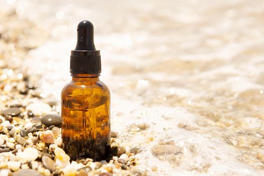 Cosmetic serum for the skin in a glass bottle. A bottle with an eyedropper on a pebble beach by the sea. Essences for skin care on the background of stones. The concept of natural cosmetics and SPA products.