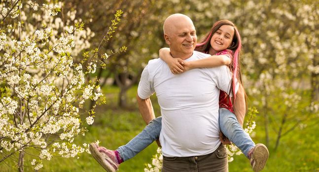 happy granddaughter hugging her smiling grandfather on green lawn.