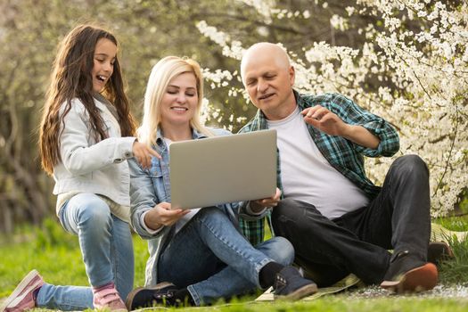 grandfather granddaughter and daughter with laptop in the garden.