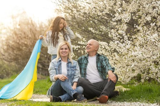 family with large flag of Ukraine in hands against background of a blooming trees. Patriotic education. Pride, freedom.