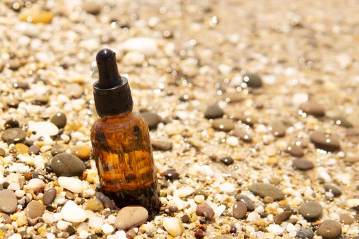 Cosmetic serum for the skin in a glass bottle. A bottle with an eyedropper on a pebble beach by the sea. Essences for skin care on the background of stones. The concept of natural cosmetics and SPA products.