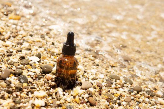 Cosmetic serum for the skin in a glass bottle. A bottle with an eyedropper on a pebble beach by the sea. Essences for skin care on the background of stones. The concept of natural cosmetics and SPA products.