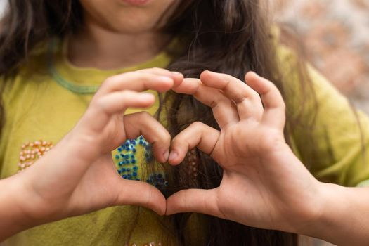 Photo of casual cheerful cute funny girl showing heart shape sign with fingers above her head.