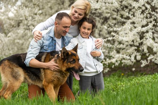 Outdoor portrait of happy young family playing in spring park under blooming tree, lovely family having fun in sunny garden.