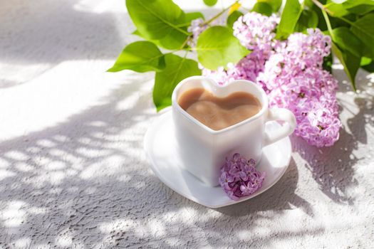 Cappuccino coffee in a cup and a branch of lilac on a white background with shadows . A hot drink. relax. The concept of cafeteria advertising. Article about cappuccino. Making cappuccino. Lilac branches. Spring. Copy space