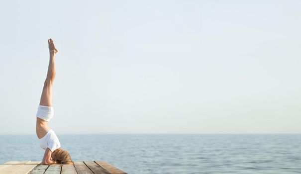 Beautiful blond woman practicing yoga at seashore and meditating