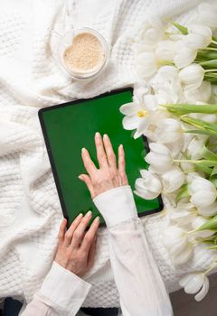 green screen tablet, young woman looking for mother's day gift online, white tulips on table, spring still life with heart shaped coffee cup, valentine's day. High quality photo