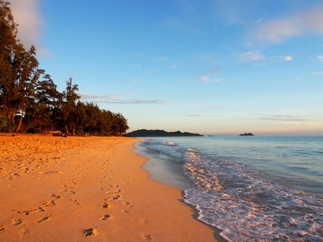 Foot prints in the sand along Waimanalo Beach at Dawn with waves lapping looking towards mokulua islands on Oahu, Hawaii.