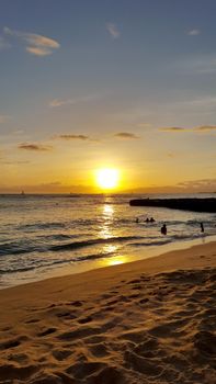 Waikiki - May 10, 2016:  Dramatic Sunset dropping behind the ocean on Kaimana Beach with boats on the water on Oahu, Hawaii. 