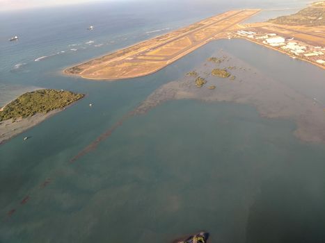 Honolulu - October 25, 2018: Aerial of Airport Reef Runway, planes and Plane hangers at Honolulu International Airport during the day with boats on the ocean on Oahu, Hawaii.