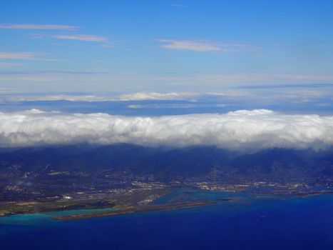 Honolulu International Airport Coral Runway and City seen from the air with surrounding water on Oahu, Hawaii and clouds over the island.  Taken on April 7, 2018.