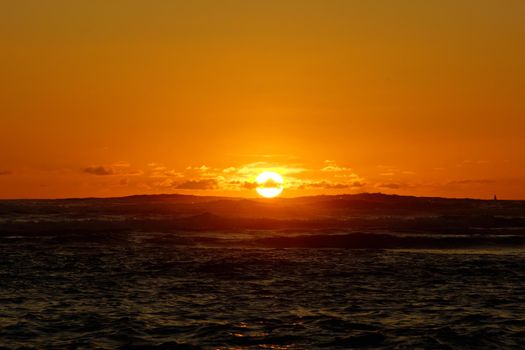 Sunset over the ocean with light reflecting on ocean waves moving with boats on the water in the distance off Waikiki with clouds on Oahu, Hawaii.