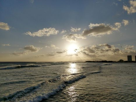 Sunset in the clouds on as wave lap towards the beach from the ocean at Ala Moana Beach Park on Oahu, Hawaii.