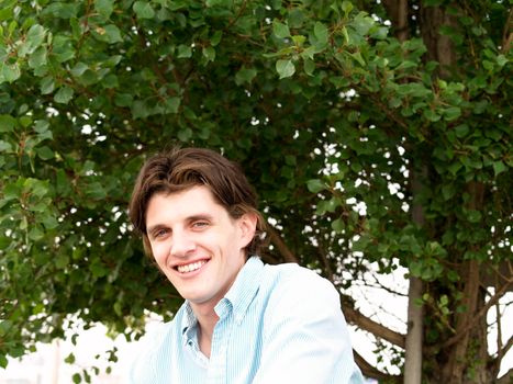 Portrait head shot of a handsome man twenty some, Actor Tony Wyban, with blue eyes and tree background.