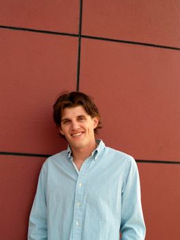 Portrait head shot of a handsome twentysome man with blue eyes against a red wall with black lines.