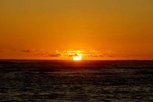 Sunset over the ocean through the clouds with light reflecting on ocean waves moving with boats on the water in the distance off Waikiki on Oahu, Hawaii.