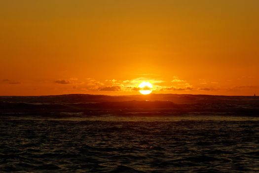 Sunset over the ocean with light reflecting on ocean waves moving with boats on the water in the distance off Waikiki with clouds on Oahu, Hawaii.