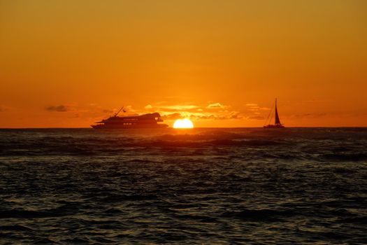 Sunset over the ocean with light reflecting on ocean waves moving with boats on the water in the distance off Waikiki with clouds on Oahu, Hawaii.