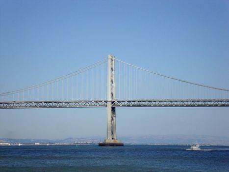 Boat passes under the San Francisco side of Bay Bridge with Oakland in the distance on a clear day.