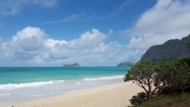 Gentle wave lap on Waimanalo Beach looking towards Rabbit island and Rock island on a nice day with clouds in the sky on Oahu, Hawaii. 