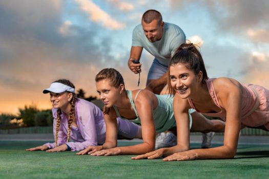 Happy fitness woman making body core planking exercise outdoors at gym. Male trainer with stopwatch. Healthy lifestyle motivation and sport concept