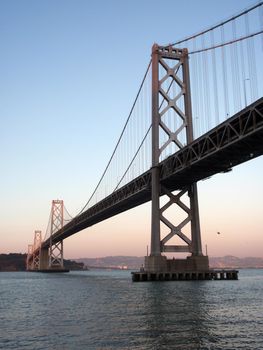 San Francisco side of Bay Bridge at dusk with bird in the air and Oakland in the distance on a clear day.